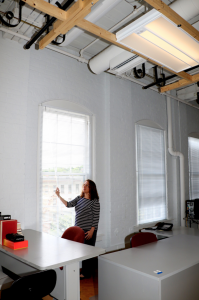 Lighting Scientist Leora Radetsky lifts the blinds and lets in the sunlight. The overhead LED luminaires dim in response, fluidly, maintaining consistent light levels on the desk spaces. PHOTO: Lighting Research Center at Rensselaer Polytechnic Institute